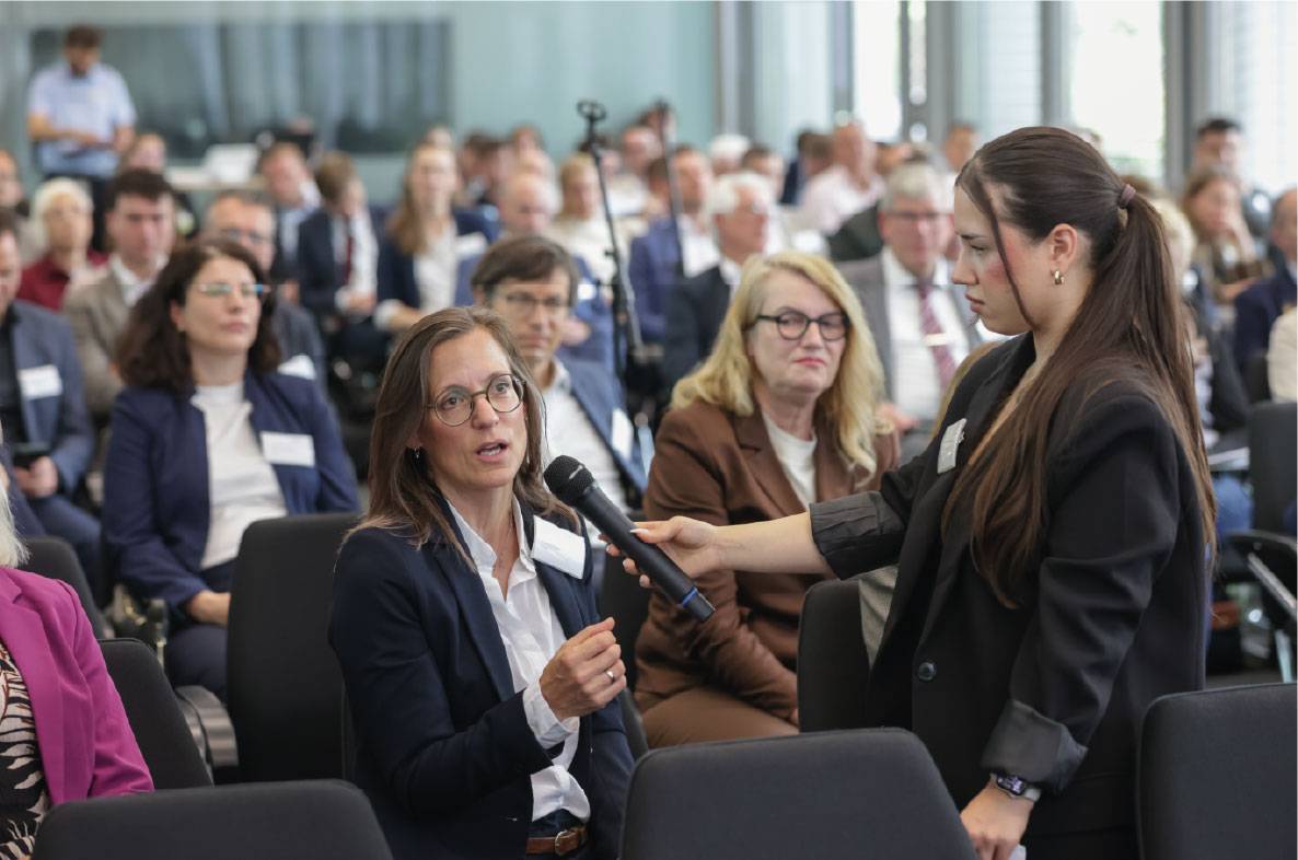 Teilnehmerin stellt während der Fragerunde auf dem 6. Außenwirtschaftsseminar der Agrar- und Ernährungswirtschaft in Bonn eine Frage an die Referenten. Eine Moderatorin hält ihr das Mikrofon, während zahlreiche Fachbesucher aus Wirtschaft, Verbänden und Politik die Diskussion verfolgen. Die Veranstaltung dient dem Austausch zu aktuellen Entwicklungen im internationalen Agrar- und Ernährungshandel sowie zu Exportchancen für deutsche Unternehmen.