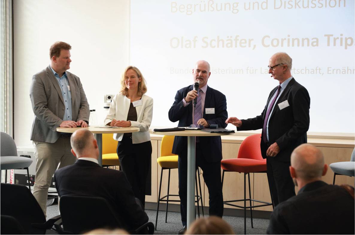Podiumsdiskussion auf dem 6. Außenwirtschaftsseminar der Agrar- und Ernährungswirtschaft in Bonn. Vier Experten aus Wirtschaft und Politik diskutieren vor Fachpublikum über aktuelle Entwicklungen im internationalen Agrar- und Ernährungshandel. Die Teilnehmer stehen auf der Bühne an Stehtischen, während zahlreiche Gäste die Diskussion verfolgen. Im Hintergrund ist eine Präsentationsfolie mit den Namen der Referenten zu sehen.