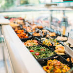 "Frische Salatbar in einem Selbstbedienungsrestaurant mit verschiedenen Schüsseln gefüllt mit Salaten, Gemüse, Brot und anderen Beilagen. Kleine Schilder mit Beschriftungen stehen vor den Speisen.