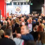 Menschenmenge auf der internationalen Süßwarenmesse ISM. Besucherinnen und Besucher bewegen sich durch die Messegänge, umgeben von farbenfrohen Ständen und Ausstellungsflächen. Die Szene zeigt das lebendige Treiben auf einer der größten Fachmessen für Süßwaren und Snacks.
