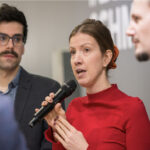 Stefanie Sabet, Geschäftsführerin der Bundesvereinigung der Deutschen Ernährungsindustrie (BVE), spricht auf der Grünen Woche in ein Mikrofon. Sie trägt ein rotes Oberteil und wird von zwei Gesprächspartnern flankiert. Die Szene zeigt einen Moment aus einer Diskussionsrunde oder einem Fachpanel.