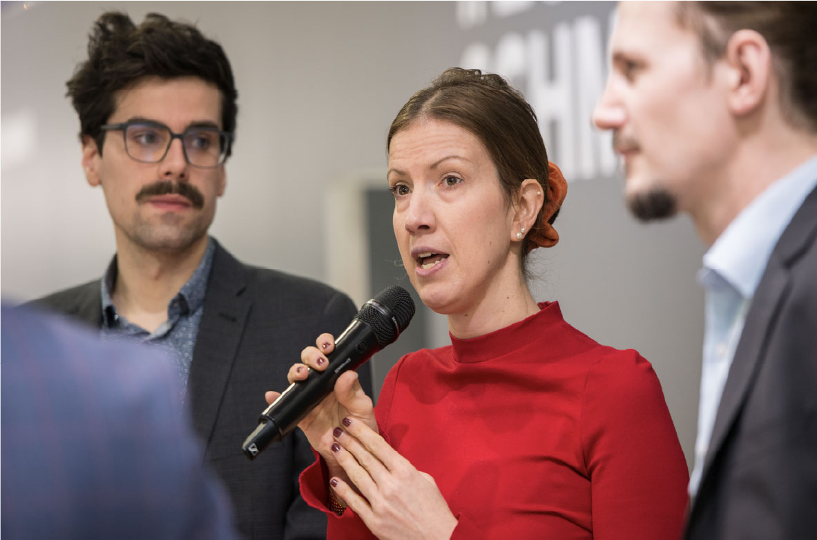 Stefanie Sabet, Geschäftsführerin der Bundesvereinigung der Deutschen Ernährungsindustrie (BVE), spricht auf der Grünen Woche in ein Mikrofon. Sie trägt ein rotes Oberteil und wird von zwei Gesprächspartnern flankiert. Die Szene zeigt einen Moment aus einer Diskussionsrunde oder einem Fachpanel.
