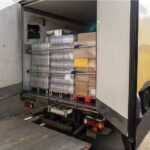 Geöffneter Lkw mit Ladefläche, auf der palettenweise abgepackte Lebensmittel wie Wasserflaschen und Kartons gestapelt sind. Die Szene symbolisiert eine Lieferung von Lebensmittelspenden, etwa an soziale Einrichtungen oder Hilfsorganisationen.