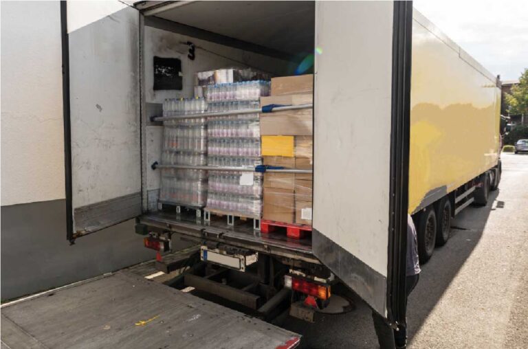 Geöffneter Lkw mit Ladefläche, auf der palettenweise abgepackte Lebensmittel wie Wasserflaschen und Kartons gestapelt sind. Die Szene symbolisiert eine Lieferung von Lebensmittelspenden, etwa an soziale Einrichtungen oder Hilfsorganisationen.