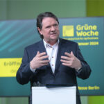 Christoph Minhoff, Hauptgeschäftsführer der Bundesvereinigung der Deutschen Ernährungsindustrie (BVE), spricht auf der Eröffnungspressekonferenz der Grünen Woche 2024 in Berlin. Im Hintergrund ist ein Bildschirm mit dem Logo der Messe und Veranstaltungshinweisen zu sehen.