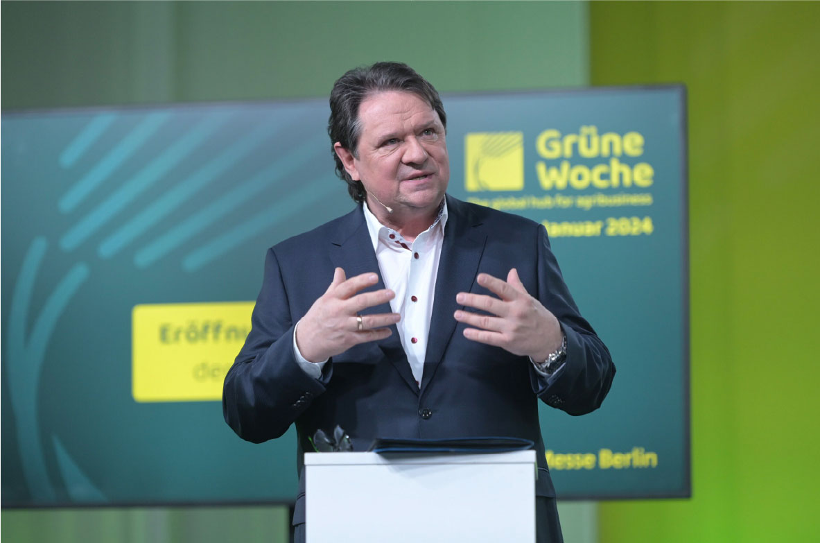 Christoph Minhoff, Hauptgeschäftsführer der Bundesvereinigung der Deutschen Ernährungsindustrie (BVE), spricht auf der Eröffnungspressekonferenz der Grünen Woche 2024 in Berlin. Im Hintergrund ist ein Bildschirm mit dem Logo der Messe und Veranstaltungshinweisen zu sehen.