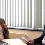Zwei Männer im Gespräch bei einem Interview oder einer Diskussion. Rechts im Bild: Peter Feller, stellvertretender Hauptgeschäftsführer der BVE. Beide tragen Mikrofone und sitzen sich an einem Tisch mit Unterlagen gegenüber. Im Hintergrund vertikale Jalousien vor einem Fenster.