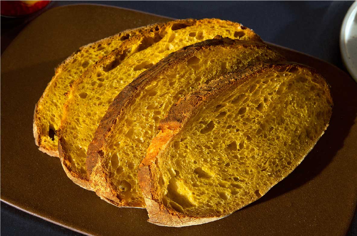 Nahaufnahme von mehreren Scheiben Solein-Brot auf einem braunen Teller. Das Brot hat eine goldgelbe Krume mit luftiger Porung und eine knusprige Kruste.
