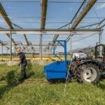 Zwei Männer arbeiten mit Rechen auf einer Versuchsackerfläche unter einem Gerüst aus Metallstreben, daneben ein blauer Traktor – aufgenommen auf der Versuchsstation Bad Lauchstädt, wo künftige Klimabedingungen simuliert und Auswirkungen auf die Landwirtschaft erforscht werden.