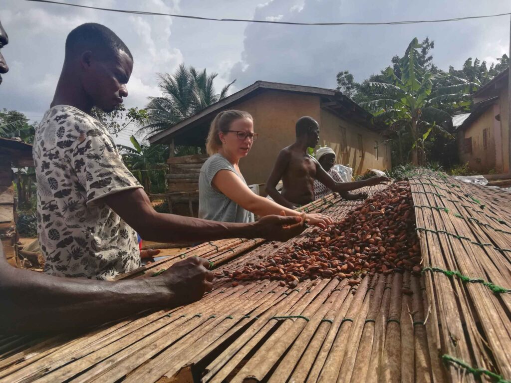 Kakaobauern und Beraterin bei der Trocknung von Kakaobohnen in einem Dorf, nachhaltige Kakaoproduktion vor Ort.