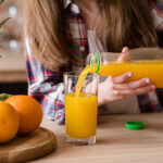 Frau gießt Orangensaft aus Plastikflasche in ein Glas.