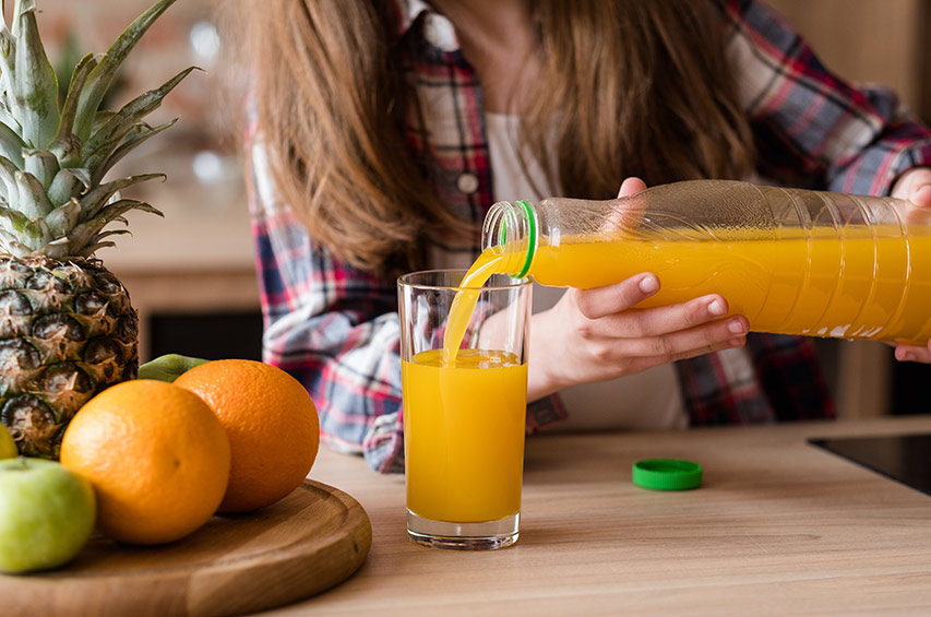 Frau gießt Orangensaft aus Plastikflasche in ein Glas.