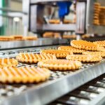 Frisch gebackene Waffeln laufen auf einem Förderband durch eine industrielle Backstraße in einer modernen Produktionsanlage.