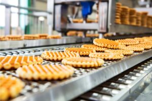 Frisch gebackene Waffeln laufen auf einem Förderband durch eine industrielle Backstraße in einer modernen Produktionsanlage.