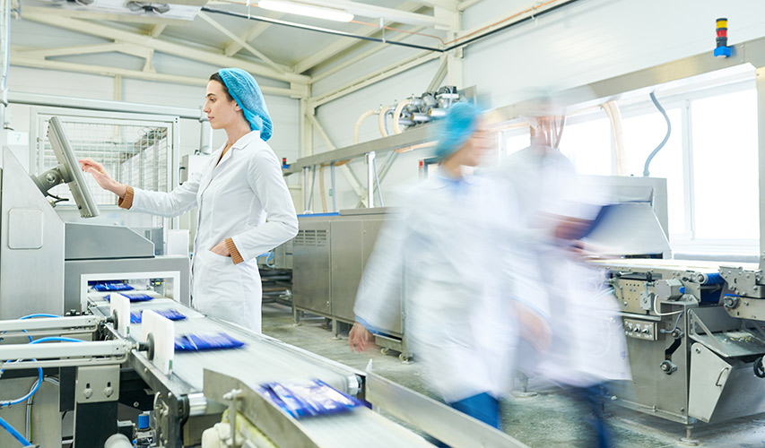 Mitarbeiterin in Hygienekleidung bedient Steuerung in einer Lebensmittelverpackungsanlage