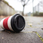 Weggeworfener Einweg-Kaffeebecher liegt auf einem nassen Gehweg.