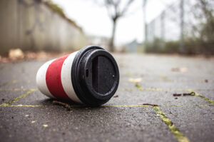 Weggeworfener Einweg-Kaffeebecher liegt auf einem nassen Gehweg.