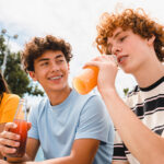 Drei Jugendliche trinken Limonade aus Glasflaschen im Freien.
