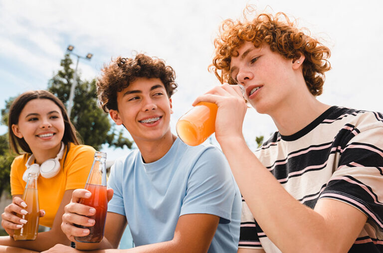 Drei Jugendliche trinken Limonade aus Glasflaschen im Freien.