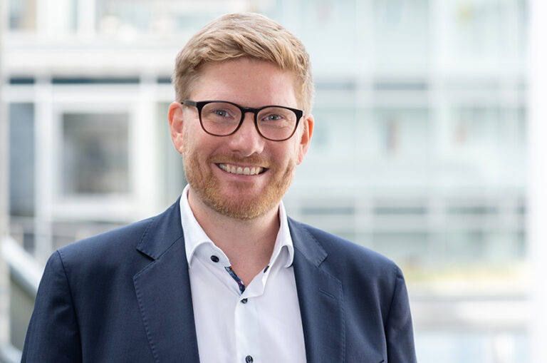 Tobias Koppitz im Porträt – lächelnd, mit Brille und Business-Outfit.