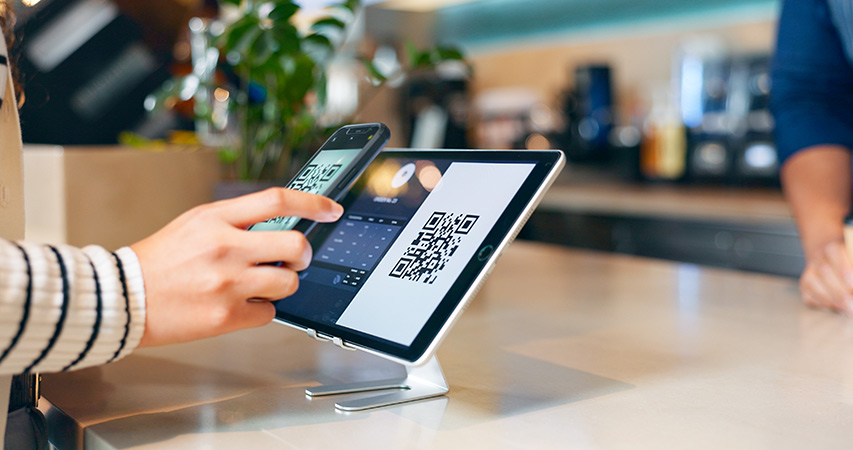 Person scannt einen QR-Code an einem Tablet, um digital zu bezahlen.