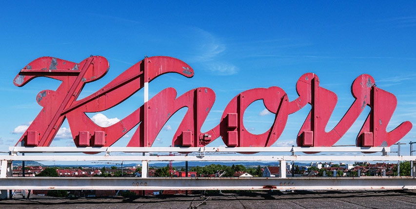 Rotes Knorr-Firmenschild auf einem Gebäudedach vor blauem Himmel.