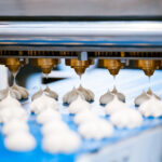 Automatisierte Dosiermaschine trägt Teigportionen auf ein Förderband in einer Lebensmittelproduktion auf.