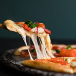 Stück Pizza mit geschmolzenem Käse als Beispiel für die Debatte um hochverarbeitete Lebensmittel und NOVA-Kritik