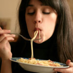 Frau isst Spaghetti von einem Teller in gemütlicher Atmosphäre