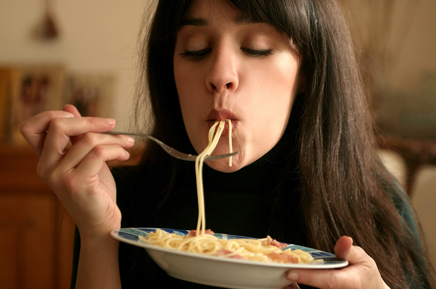 Frau isst Spaghetti von einem Teller in gemütlicher Atmosphäre