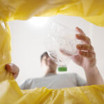 Verbraucher wirft leere Plastikflasche in eine gelbe Tonne zur Mülltrennung