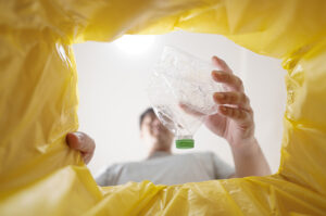 Verbraucher wirft leere Plastikflasche in eine gelbe Tonne zur Mülltrennung
