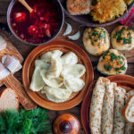 Tisch mit osteuropäischen Speisen wie Teigtaschen, Suppe und Brot.