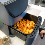 Airfryer mit gebackenen Kartoffelspalten im Korb auf Küchenarbeitsplatte