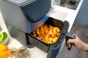Airfryer mit gebackenen Kartoffelspalten im Korb auf Küchenarbeitsplatte