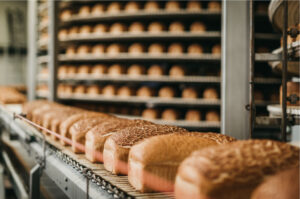 Frisch gebackene Brote auf einem Förderband in einer modernen Großbäckerei: Automatisierte Produktion von Backwaren in der Lebensmittelindustrie mit industrieller Verarbeitung und Verpackung frischer Brotprodukte.