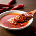 Löffel mit Chiliöl und Chiliflocken über einer Schale mit scharfer Sauce