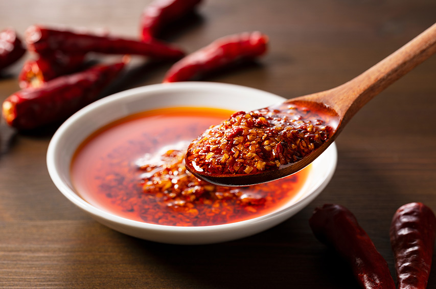 Löffel mit Chiliöl und Chiliflocken über einer Schale mit scharfer Sauce