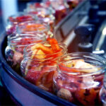 Paprika wird in Gläser abgefüllt, die auf einem Fließband stehen.