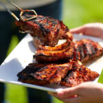 Gegrilltes Fleisch und Würstchen auf einem Teller beim Grillen im Freien.