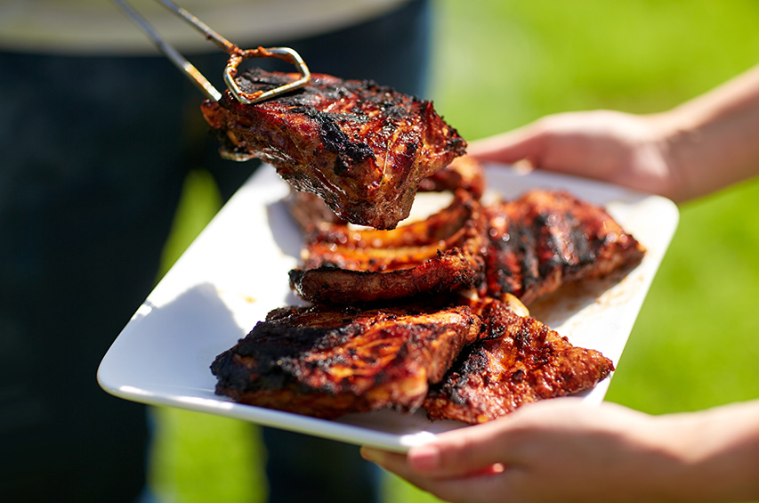 Gegrilltes Fleisch und Würstchen auf einem Teller beim Grillen im Freien.