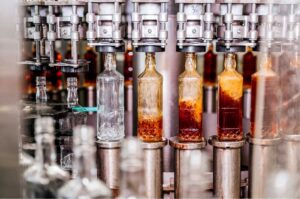 Automatisierte Abfüllanlage in der Getränkeindustrie mit Glasflaschen auf einem Förderband während des Abfüll- und Verpackungsprozesses alkoholischer Getränke in einer modernen Produktionshalle.