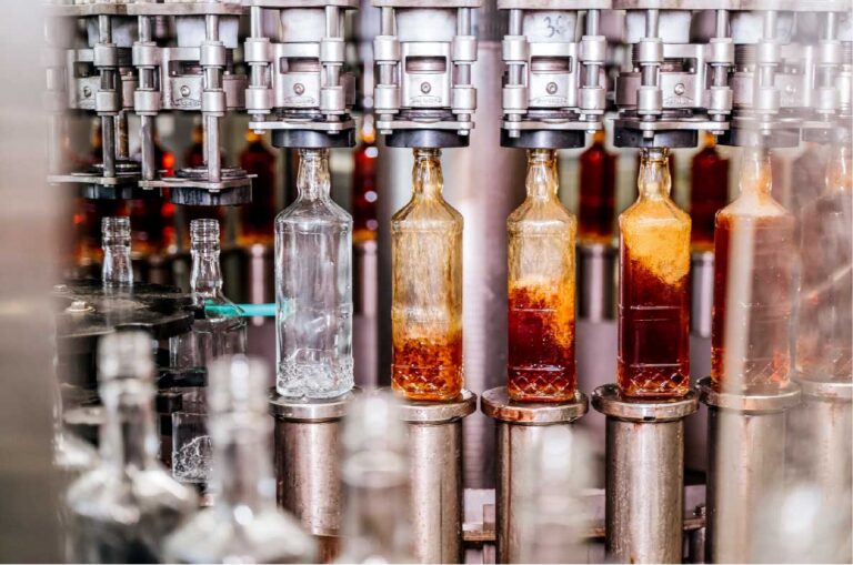 Automatisierte Abfüllanlage in der Getränkeindustrie mit Glasflaschen auf einem Förderband während des Abfüll- und Verpackungsprozesses alkoholischer Getränke in einer modernen Produktionshalle.