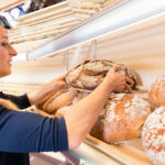 Bäckereifachverkäuferin greift Brot aus dem Regal einer deutschen Bäckerei