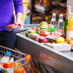 Frau legt Lebensmittel an der Supermarktkasse aufs Band.