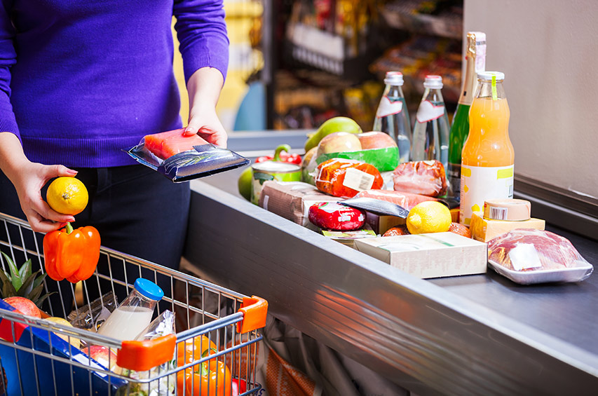 Frau legt Lebensmittel an der Supermarktkasse aufs Band.