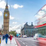 Blick auf den Big Ben und das Westminster-Viertel in London mit einem vorbeifahrenden roten Doppeldeckerbus