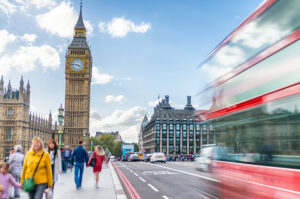 Blick auf den Big Ben und das Westminster-Viertel in London mit einem vorbeifahrenden roten Doppeldeckerbus