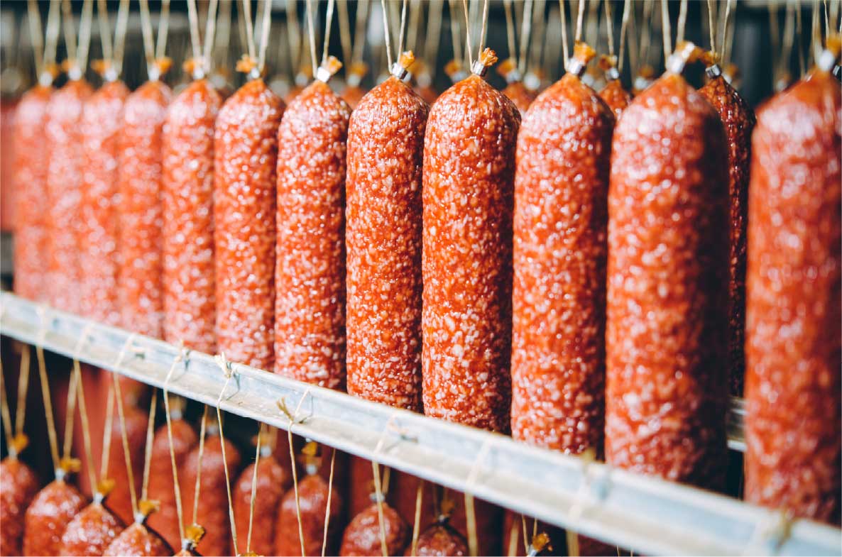 Industrielle Produktion von Wurstwaren: Reihen von Salami oder Rohwürsten in einem lebensmittelverarbeitenden Betrieb.