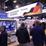 Besucherinnen und Besucher auf einem gut besuchten Messestand der Bundesvereinigung der Deutschen Ernährungsindustrie auf der Anuga. Über dem Stand hängt ein großes Banner mit der Aufschrift „Food & Drink Industries Germany“. Im Vordergrund ist moderne Lebensmitteltechnologie zu sehen, während zahlreiche Fachbesucher durch die Messehalle gehen. Das Bild steht für Export, Innovation und die internationale Präsenz der deutschen Ernährungsindustrie.